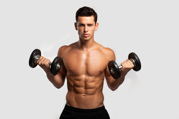Fototapeta na wymiar Front image of a confident young man with bare torso, training with dumb-bell, isolated white background. Horizontal view.