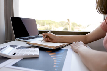 Businesswoman bookkeeper hand note analysis the graph with calculator and laptop at the home office for setting challenging business goals And planning to achieve the new target