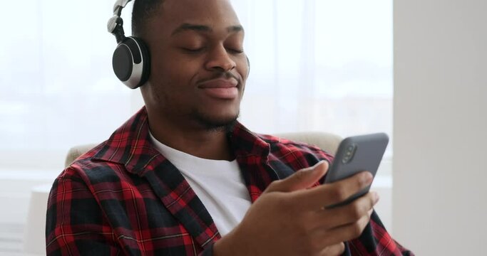 Happy man listening music using mobile phone and headphones at home