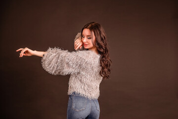 beautiful girl poses on a black gray background. lady in jeans and grey fluffy sweater