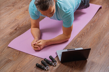 50 year old man performs exercises lying on mat at home looking at computer