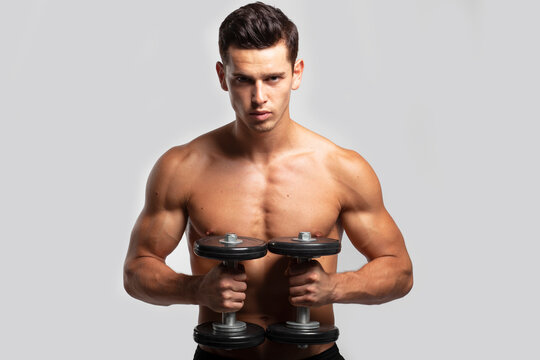 Closeup front portrait of a fit, strong handsome guy with bare torso, training with dumb-bell, isolated white background. Horizontal view.