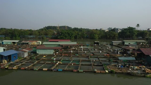 Floating fish farming community in Bien Hoa on the Dong Nai river, Vietnam on a sunny day. Drone tracking shot flying low.