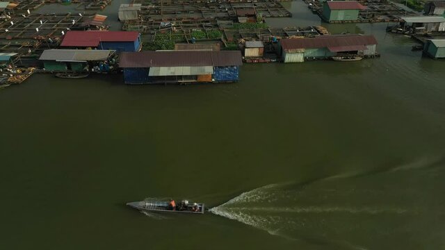 Floating fish farming community in Bien Hoa on the Dong Nai river, Vietnam on a sunny day. Drone tracking shot following a boat on the river.