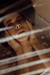 Photo portrait of pretty brunette woman with make up touching transparent cellophane covered with water drops 