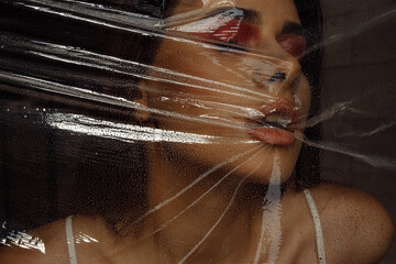 Photo portrait of brunette woman wearing make-up breathing behind transparent cellophane covered with water drops