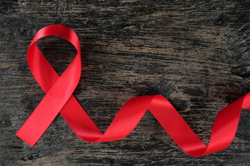 Top view of red ribbon on aged dark wood background. AIDS, HIV, heart disease and stroke awareness concept. Testing and Screening for HIV and AIDS.