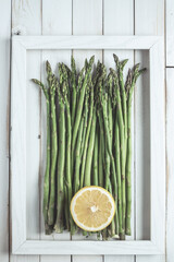 Asparagus in a frame on white old wooden board with half lemon
