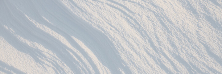 Beautiful winter background with snowy ground. Natural snow texture. Wind sculpted patterns on snow surface. Wide panoramic texture for background and design.