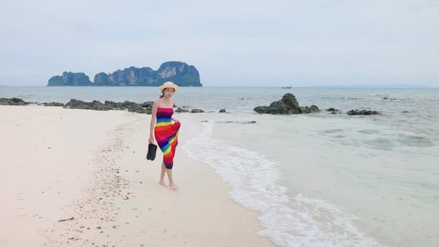 Lower body of female wear colorful beach dress enjoy playing kicking sea waves on tropical beach, crystal clear sea water, relaxing summer tropical paradise island beach vacation, waves hitting feet