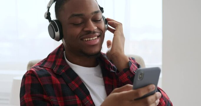 Happy man singing while listening music using mobile phone and headphones at home