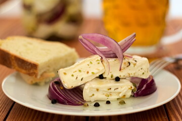 Camembert marinated in oil with red onion, spice and herbs. Presented on a white plate with bread.