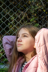 teenage girl in pink jacket looks up dreamily on a sunny day.