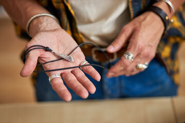 jeweler man's hands holding handmade chains, creative guy in csaual wear in workshop, skilled and talented. close-up hands