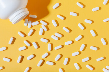 White pills are poured from a jar on a yellow background. Food supplement, multivitamins, medications