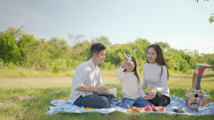 Happy family asian and little girl playing the toy airplane and have enjoyed ourselves together during picnicking on a picnic cloth in the green garden. Family enjoying sunny fall day in nature.