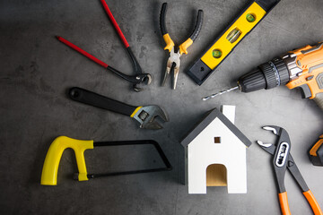 Wooden white house toy and construction tools on Gray-black cement floor background with copy space.Real estate concept, New house.Home repair concept