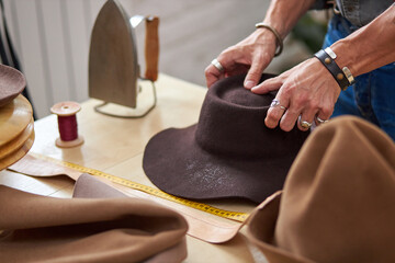hat sewing by designer in workshop, cropped male making handmade hats, professional atelier giving...
