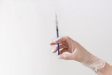 Female arm in vinyl transparent glove holding needle above white background.