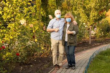 Senior couple embracing in spring or summer park wearing medical mask