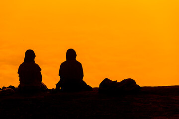 silhouette of Couple Muslim woman hijab head covering. Sitting and Looking Over Mountains at sunrise with foggy
