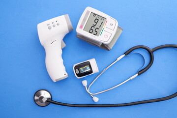 Blood pressure monitor, oximeter, digital thermometer and stethoscope on blue background