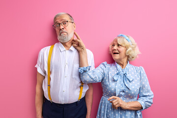 joyful woman have fun with husband , playing with gray-haired man isolated on pink background, index finger at man's face