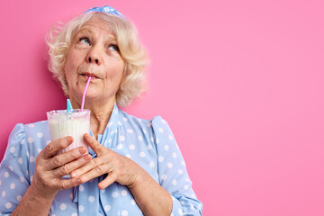 senior woman drinking milk cocktail isolated over pink background, portrait. people, lifestyle concept