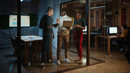 Diverse Multiethnic Team are Having a Conversation in a Meeting Room Behind Glass Walls in an Office. Black Creative Director Talks to Project Managers About the Work and Shows Brief on Laptop.