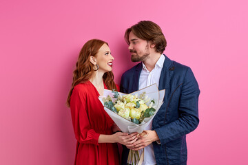 affectionate man offering his partner roses on pink background, lovely couple celebrating their...