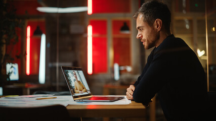 Handsome Caucasian Project Manager is Making a Video Call on Laptop Computer in a Creative Office Environment. Male Specialist Talking to a Multiethnic Latina Colleague Over a Live Camera.