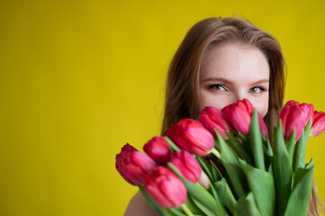Fototapeta premium Woman with a bouquet of red tulips on a yellow background. Happy girl in a black dress holds an armful of flowers . Gift for Valentine's Day. The most romantic day of the year.