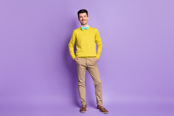 Fototapeta premium Full size photo of brunet optimistic guy stand hands in pockets wear yellow sweater trousers sneakers isolated on lilac background