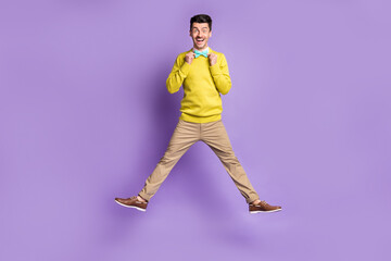 Fototapeta na wymiar Full size photo of brunet optimistic guy jump wear yellow sweater trousers sneakers isolated on lilac background