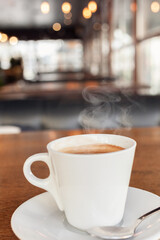 Coffee in a cafe on a wooden table. Drink with steam, smoke. Beautiful blurry background with sideways. Sunlight, interior. Delicious Hot Americano