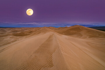 Full moon over the sand dunes in the desert. Arid landscape of the Sahara desert