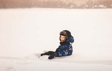 Fototapeta na wymiar Cute little boy sits in the snow in winter