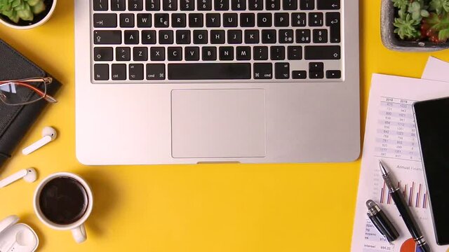 Yellow office desk with laptop, reports and gadgets top view zoom in. Cropped shot
