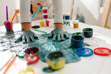 Child painting her hand with paint and paintbrush. Art therapy for children.