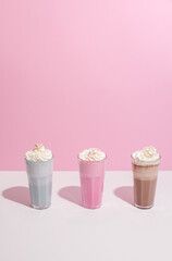 Strawberry, chocolate and vanilla milkshake with whipped cream on pink background. Place for text. Sweet drinks
