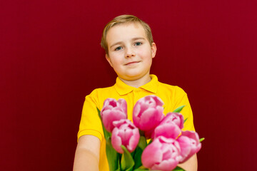 Boy Giving Flowers Bouquet, Kid holding Purple Tulips Bunch,Looking at Camera.Studio shot. Burgundy background.