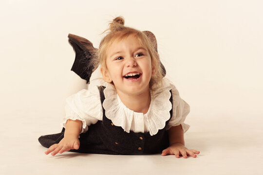 cute little blond baby girl in black dress laughing lay on floor