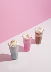 Strawberry, chocolate and vanilla milkshake with whipped cream on pink background. Place for text. Sweet drinks