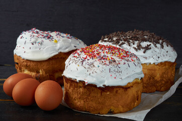 Traditional Easter bread or cake with white glaze and multicolored rainbow sprinkle decorated with eggs on the black wooden background. Close up view