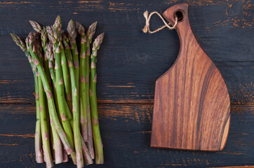 Fresh green asparagus bunches on black wooden background decorated with brown board. Top view copy space 