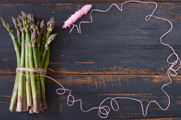 Fresh green asparagus bunch decorated with pink thread on the black wooden background. Top view with copy space