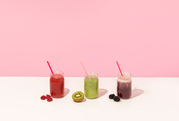 Summer colorful fruit smoothies in jars on pink background. Healthy, detox and diet food concept. Copy space