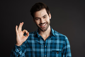 Joyful handsome unshaven guy smiling and showing ok sign