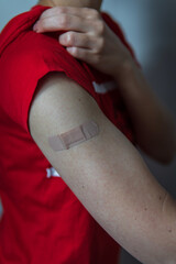 A woman showing her arm with an adhesive bandage after injection of vaccine or a scratch on the skin. First aid. Medical, pharmacy, and healthcare concept. After vaccination treatment. Pop up colors.