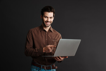 Joyful handsome guy using and pointing finger at laptop